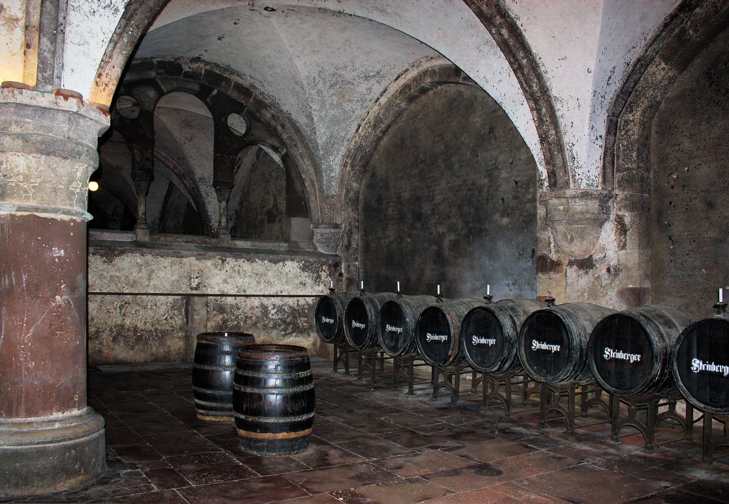Rows of wooden wine barrels in the vaulted stone cellar of Eberbach Abbey