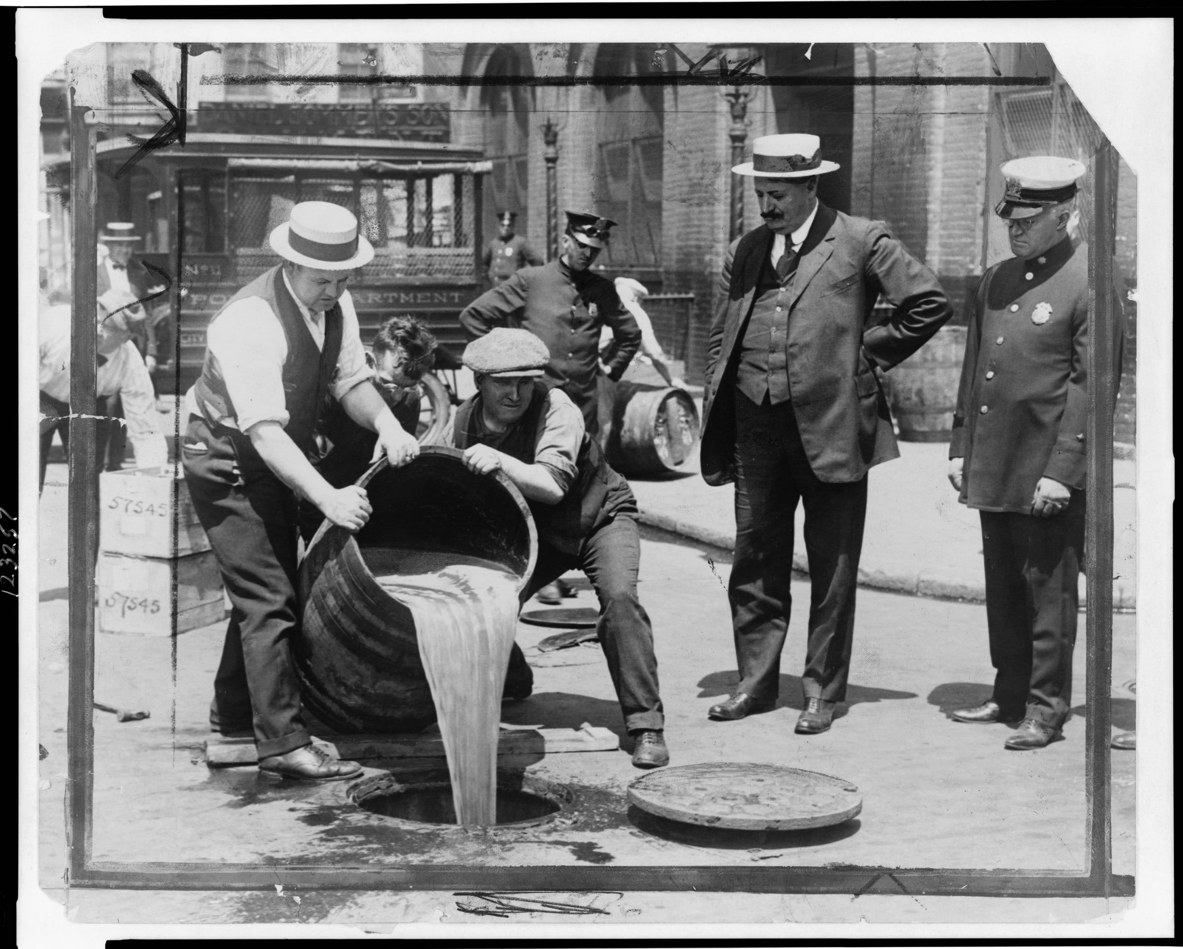 Prohibition agents empty a barrel of liquor into a New York street sewer while officials in suits look on